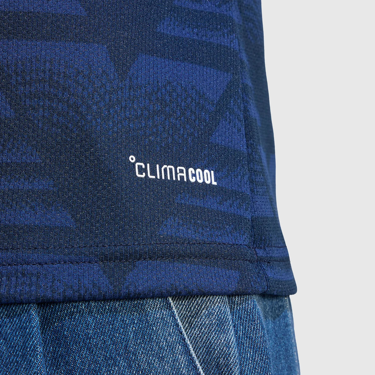 Close-up of a blue patterned athletic top with the white 'CLIMA COOL' logo, paired with blue denim shorts against a light gray background.