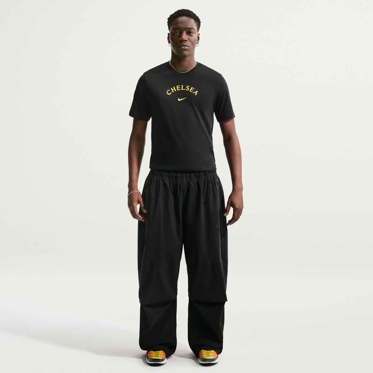 Man wearing a black 'Chelsea' t-shirt and black pants on a white background