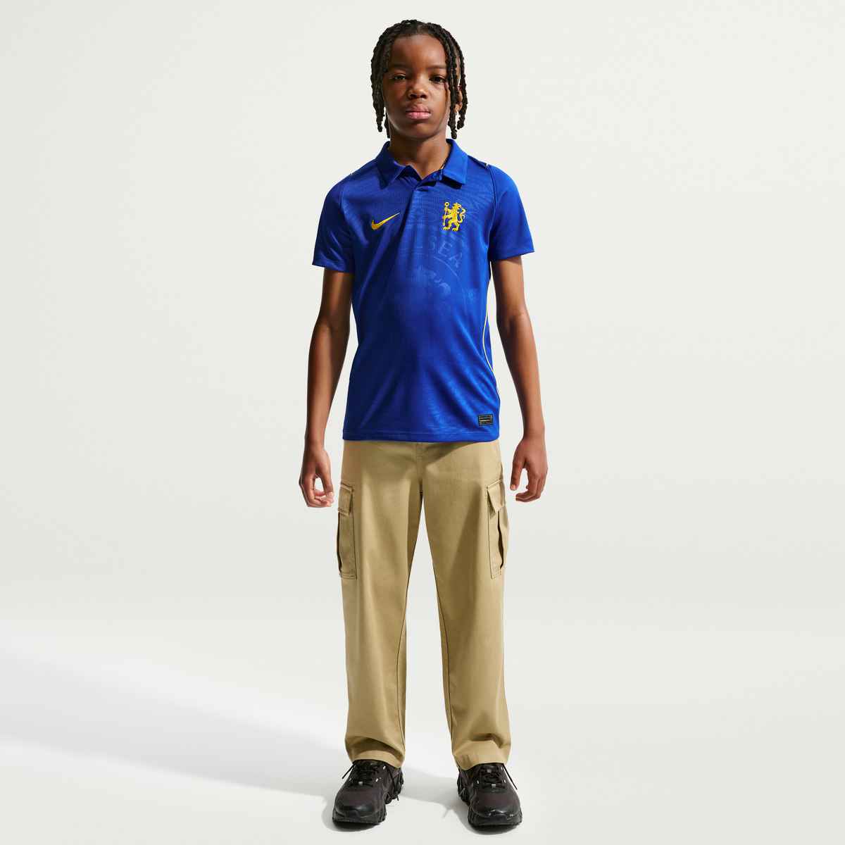 Child wearing a blue polo shirt with a logo and beige pants on a white background